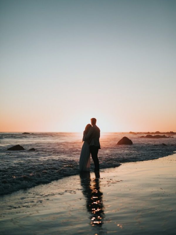 silhouette photo of couple standing on beach watching sunset